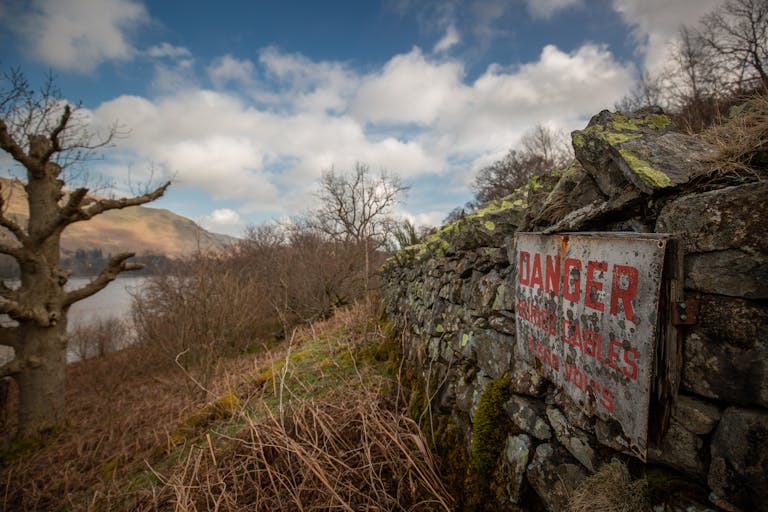 A scenic view with a rustic stone wall, danger sign, and bare trees near a lake.